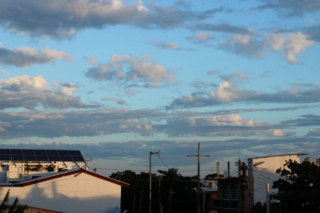 A scenic view of rooftops with solar panels under a cloudy blue sky during the day.